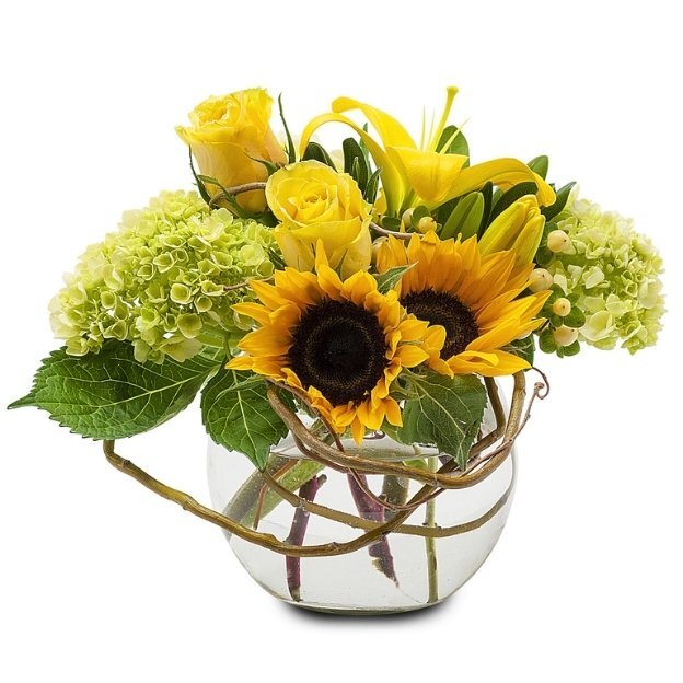 Glass vase bouquet with sunflowers, yellow roses, green hydrangeas, and lush greenery arranged in a round container.