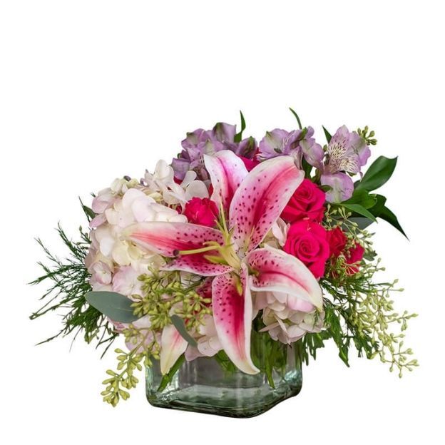 Square glass vase arrangement with a pink lily, pink roses, pale hydrangeas, and greenery.